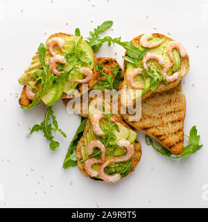 Gesunde leckere Snacks. Toast mit Avocado, Garnelen und Rucola auf weißem Hintergrund. Ansicht von oben, flach. Stockfoto