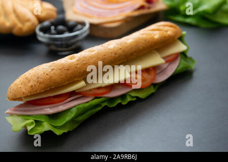 Sandwich mit Baguette, Schinken, Salat, Tomaten auf dunklem Hintergrund. Frühstück oder Fast Food. Stockfoto