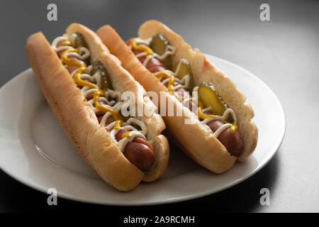 Hausgemachte heiße Hunde mit Würstchen und Eingelegtes cucubers in der Platte, isoliert. Stockfoto