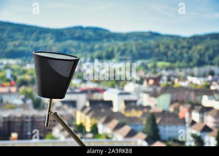 Eine moderne flexible Tischleuchte nach oben vor einem Fenster mit Stadtbild und die Berge im Hintergrund an einem sonnigen Tag Stockfoto