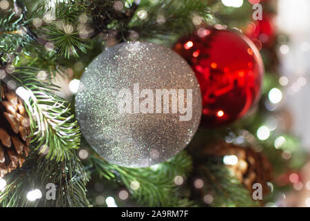 Geschmückten Weihnachtsbaum Nahaufnahme. Rote und silberne Kugeln und Girlande mit Beleuchtung. Neues Jahr Foto mit Bokeh. Winterurlaub Licht Dekoration. Stockfoto