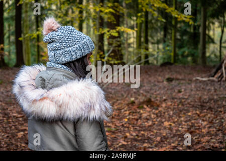Eine Frau in den 30er steht allein in einem Wald in einem Winter Küste und gestrickte Bobble hat Stockfoto