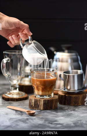 Frau Hand gießen Kokoscreme in vietnamesischen Filterkaffee in Glas auf Holz Tafel auf dunklem Hintergrund Kopie Raum Stockfoto