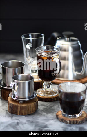 Vietnamesische schwarze tropfen Eis Kaffee in irischen Becher mit phin und Schwanenhals Wasserkocher auf schwarzen Hintergrund selektiven Fokus Stockfoto