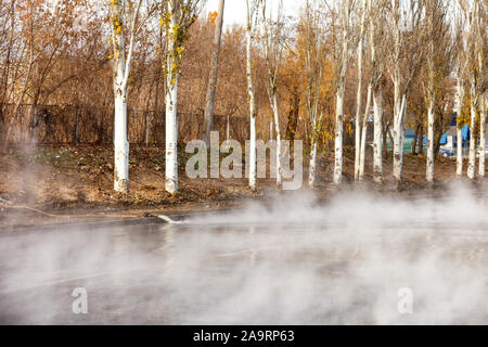 Ein Durchbruch in einem Rohr mit heißem Wasser, das Wasser ist auf die Straße mit einer Pumpe und einem Schlauch gepumpt, bilden ein Dampf Dunst über dem Asphalt. Stockfoto