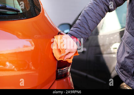 Mann nach Reinigungstücher seine orange Auto mit einem Lappen am Auto waschen. Männliche Hand und Karosserie Nahaufnahme. Stockfoto