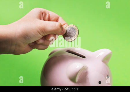 Ein Kind einen Euro in ein Sparschwein. Wir unterrichten Kinder aus der Kindheit für den Ruhestand zu sparen und verlassen sich nur auf sich selbst Stockfoto