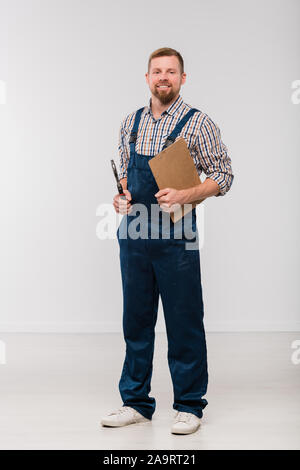 Glückliche junge Mechaniker in Overalls und Shirt holding Zwischenablage und Handwerkzeug Stockfoto