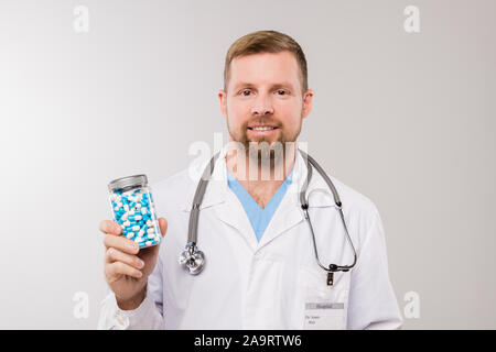 Glückliche junge Bartgeier Kliniker mit Stethoskop holding Flasche mit Pillen Stockfoto
