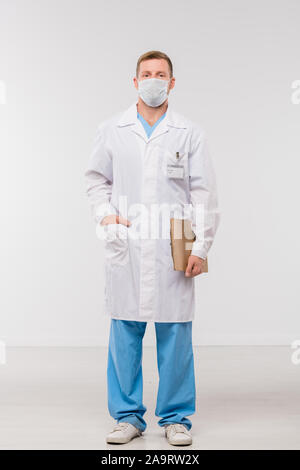 Junge Kliniker in Jungtieren, einheitliche und Schutzmaske holding Dokument Stockfoto