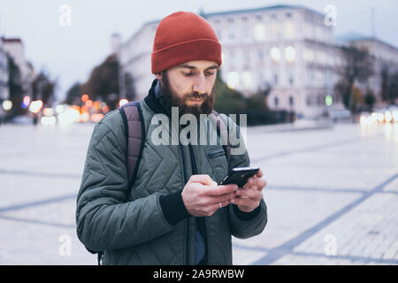 Junge Bartgeier kaukasischen Mann suche auf Mobiltelefon beim Gehen auf die Straße Stockfoto