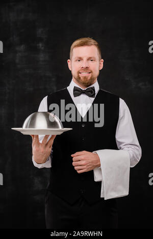 Glückliche junge elegante Kellner mit weißen Handtuch und Cloche mit Nahrungsmitteln Stockfoto