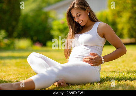 Lächelnd schwangere Frau sitzt auf dem Rasen in Ihrem Garten Stockfoto