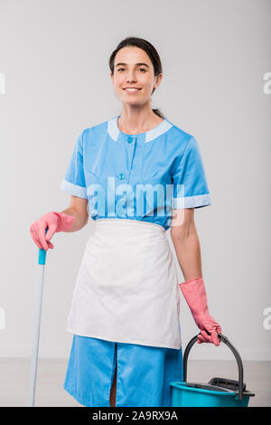 Glückliche junge Hotelpersonal in Uniform und Gummihandschuhe holding Schaufel und mop Stockfoto