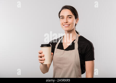 Happy brünette Kellnerin in Schürze bietet Ihnen Glas Kaffee oder Milch cocktail Stockfoto