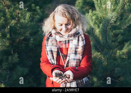Junge blonde Caucasian woman holding Weihnachtsbaum Kiefernzapfen in Ihren Händen Stockfoto