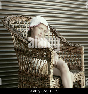 Schöne kleine Kaukasische Mädchen sitzen in einem großen Korbstuhl, als vintage Foto in Kaffee Farbe bearbeitet Stockfoto