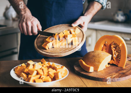 Mann schneidet orange Kürbis in der Küche zu Hause. Stockfoto