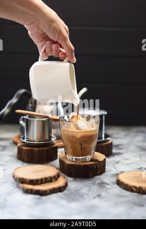 Die eiskaffee mit Kokosmilch vietnamesischen Stil. Frau hand Kaffee Gießen auf Eis auf dunklem Hintergrund Kopie Raum Stockfoto