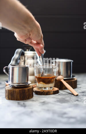 Die filterkaffee in phin vietnamesischen Stil. Hand rühren Kaffee und Kondensmilch auf dunklem Hintergrund Kopie Raum Stockfoto