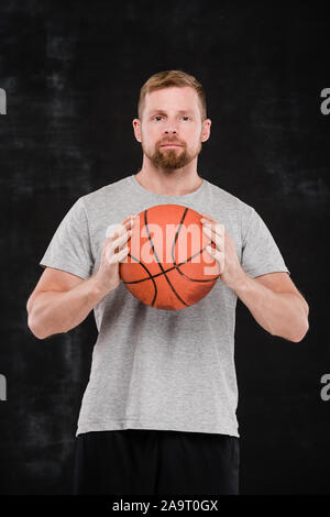 Junge erfolgreiche Basketballspieler in Sportswear holding Ball von der Brust Stockfoto