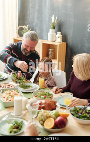 Gerne reifer Mann, der Salat zu seinem adorable Enkelin von festlichen Tisch Stockfoto