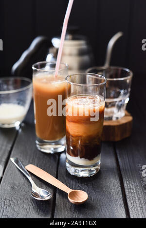 Iced geschichteten Kaffee mit Kokosmilch und Kondensmilch in hohe Gläser vietnamesischen Stil auf dunklem Hintergrund vertikal Stockfoto