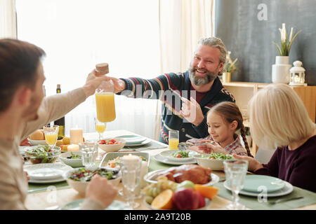 Gerne älterer Mann vorbei Flasche Orangensaft zu seinem Sohn über serviert Tabelle Stockfoto