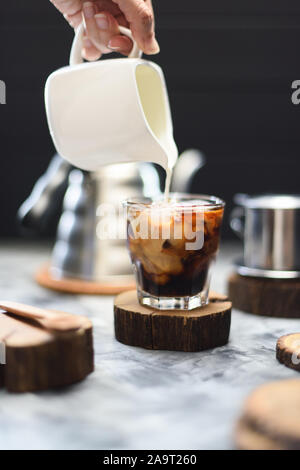 Die schwarzen Eiskaffee mit Kokosmilch vietnamesischen Stil. Frau hand Kaffee Gießen auf Eis auf dunklem Hintergrund Kopie Raum Stockfoto