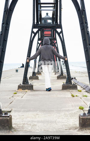 Hooded Frau gehen an einem Pier in Richtung Leuchtturm am Lake Michigan. Verbringen mehr Zeit im Freien. Stockfoto