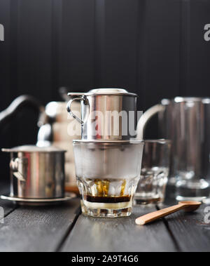 Preraring Filterkaffee vietnamesischen Stil. Heißer Schwarzer Kaffee tropft aus Kaffeemaschine phin in Glas auf schwarzem Hintergrund Kopie Raum Stockfoto