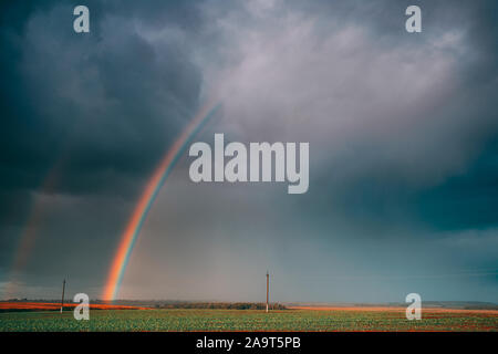 Dramatische Himmel bei Regen mit Regenbogen am Horizont über ländliche Landschaft Feld. Agrar- und Wettervorhersage Konzept. Landschaft Wiese im Herbst Stockfoto