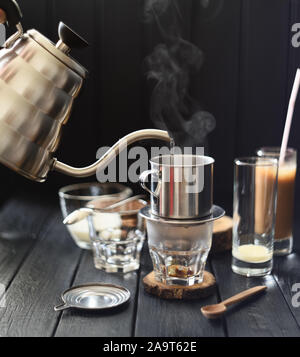 Die vietnamesischen Filterkaffee. Gießen dampfenden Wasser in phin von Schwanenhals Wasserkocher auf schwarzen Hintergrund Kopie Raum Stockfoto