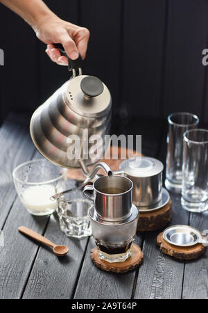 Die vietnamesischen Filterkaffee. Frau Hand strömenden heißen Wasser in phin von Schwanenhals Wasserkocher auf schwarzen Hintergrund Kopie Raum Stockfoto