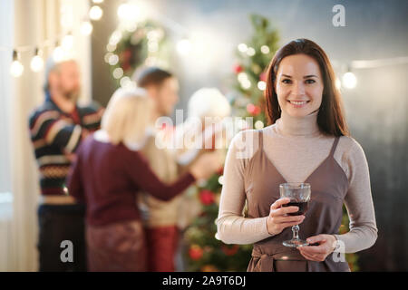 Glückliche junge brünette Frau mit Glas Wein Glückwünsche zu Weihnachten Stockfoto