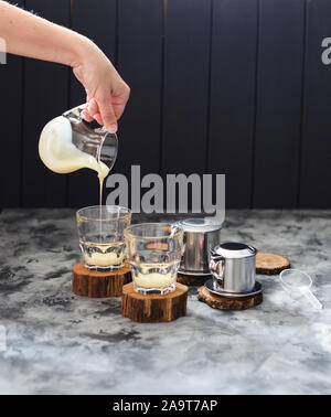 Kaffee vietnamesischen Stil. Frau Hand gießen Kondensmilch in Gläsern auf dunklem Hintergrund Kopie Raum Stockfoto