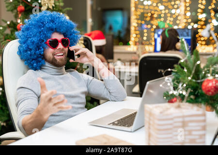 Happy Büroangestellter in Sonnenbrille und blauen Lockenperücke telefonieren Business Partner Stockfoto