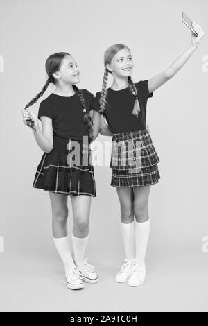 Lustige Freunde. Spaß. Schwesternschaft und Freundschaft. Glücklich wissen Tag. Kindheit Glück. Bildung Konzept. zurück zu Schule. sozialen Netzwerk. Mädchen in Uniform. kleine Mädchen selfie am Telefon. Stockfoto