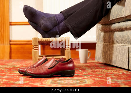 Füße auf einen Schemel keine Schuhe mit Tasse heißes Getränk für Entspannung durch Person Stockfoto