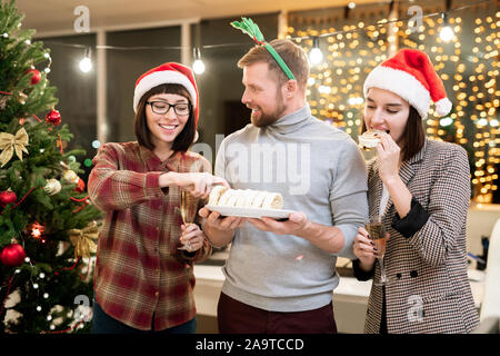 Glückliche junge Unternehmerinnen in Santa Kappen mit Dessert und Champagner Stockfoto