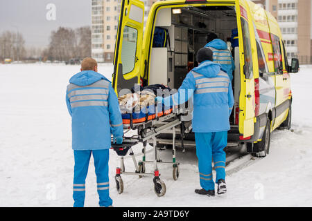 Sanitäter schieben Bahre mit festen unbewussten Mann in Krankenwagen Auto Stockfoto