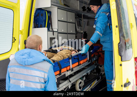 Sanitäter in Uniform drücken Bahre mit unbewussten Mann in Krankenwagen Auto Stockfoto