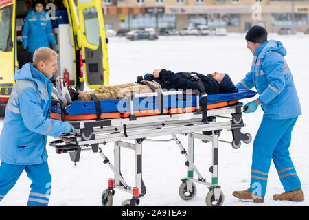 Zwei Sanitäter schieben Kranken unbewussten Mann auf der Bahre zum Krankenwagen Auto Stockfoto