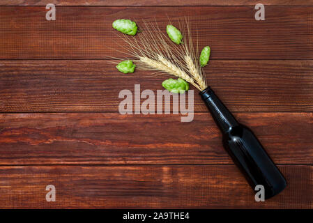 Bier in Form von Hopfen und Ähren gießt aus dem Hals der Flasche. Eine Flasche Bier mit Hopfen und Weizen ährchen auf hölzernen backgroun Stockfoto