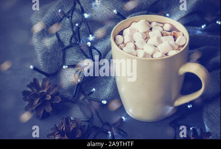 Heißer Winter Drink mit Kakao und Marshmallows in Becher auf grauem Beton Hintergrund mit Christmas Garland und Tannenzapfen. Stockfoto