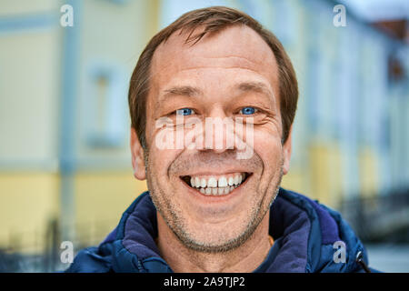 Fröhliche kaukasischen Mann im mittleren Alter über 50, close-up lächelnd Unrasierten Gesicht mit weißen Zähnen und blaue Augen. Eine glückliche weiß, männlich, 50 Jahre alt auf einem Stockfoto