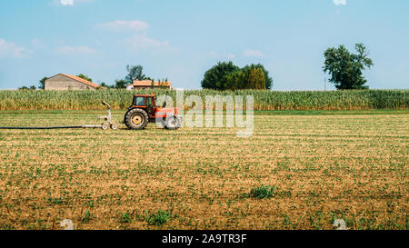 Roter Traktor mit einem Wasserschlauch im Feld in ein schönes Blau sonniger Tag. Stockfoto