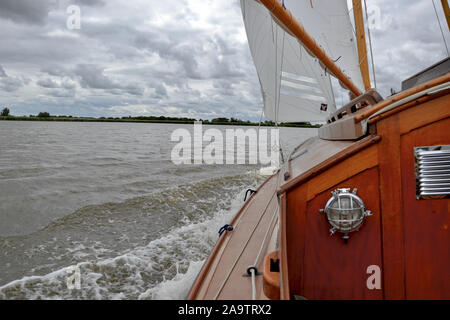 Blick aus dem Cockpit eines alten Holzhütte Yacht segeln schnell auf einem See an einem windigen, grauer Tag. Wellen blubbern um sidedeck, Segel voll. Stockfoto