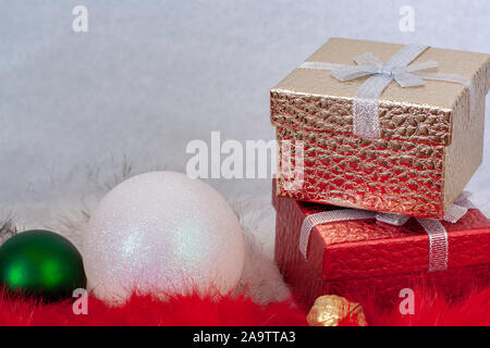 Zwei Geschenkboxen und zwei Weihnachten Kugeln auf weißen und roten Fell mit einem weißen Hintergrund. Rot und gold Boxen stehen auf der jeweils anderen. Grün und Weiß ba Stockfoto