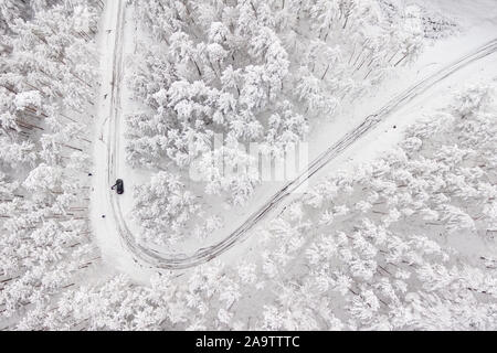 Auto auf der Straße im Winter durch einen Wald mit Schnee bedeckt. Luftaufnahmen von einer Straße im Winter durch einen Wald mit Schnee bedeckt. High Mountain Pass. Stockfoto